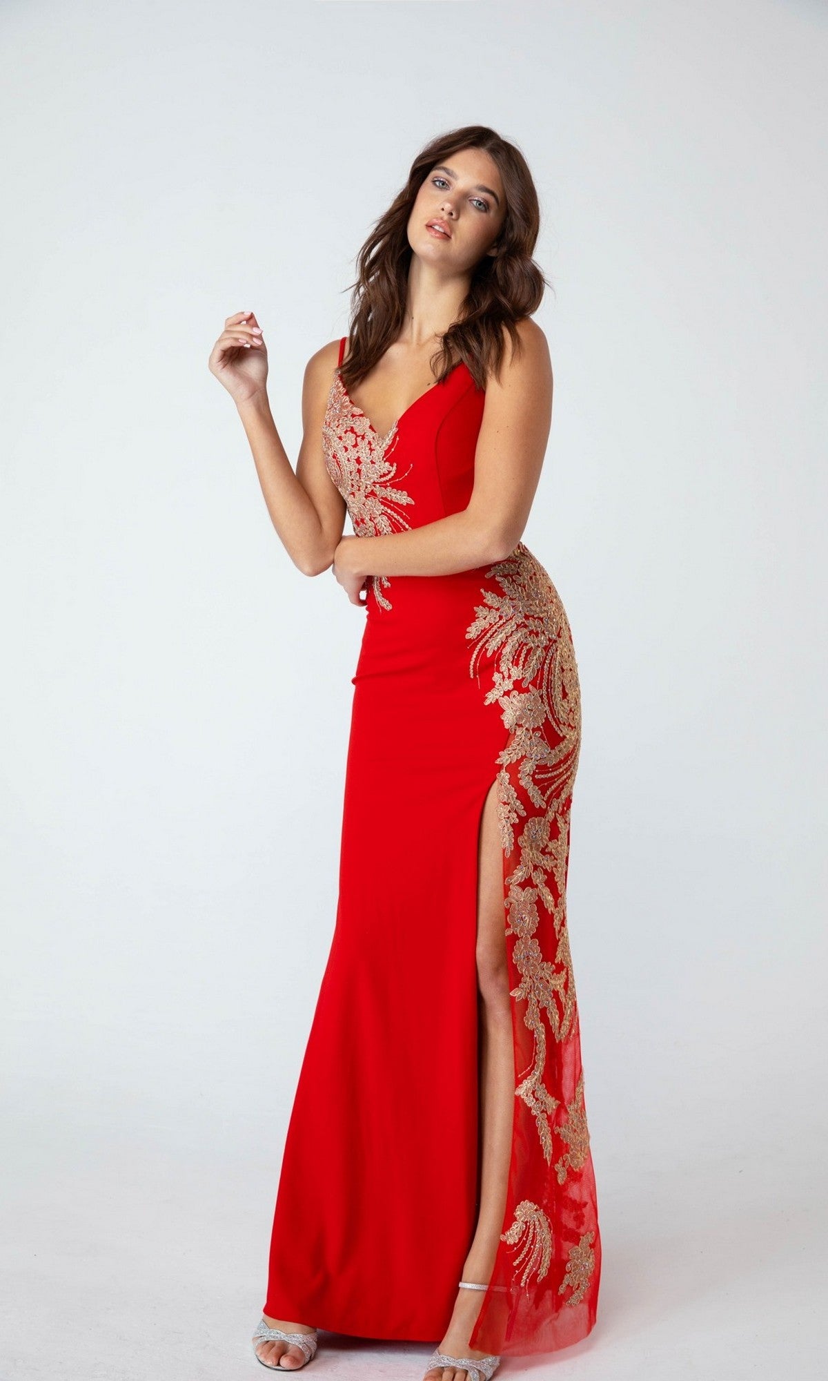 A woman models the Eureka 9996 long prom dress—fitted, sleeveless, in red with gold embroidery, lace-up open back, embroidered gold appliques, and a thigh-high slit—against a plain white background.